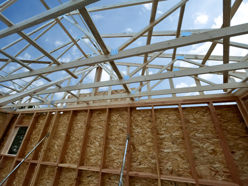 Charpente en bois d'une maison en construction, murs en OSB et fermettes de toit sous un ciel bleu.