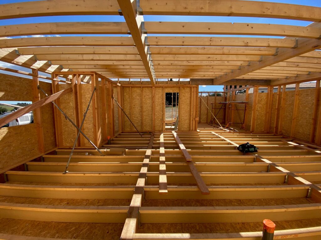 Construction maison ossature bois : intérieur du chantier Chantier d'une maison en bois : ossature, solives de plancher et murs en OSB sous un ciel bleu.