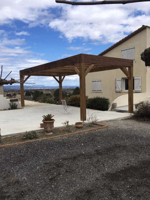 Pergola bois massif sur terrasse béton devant maison provençale avec vue panoramique sur la vallée.